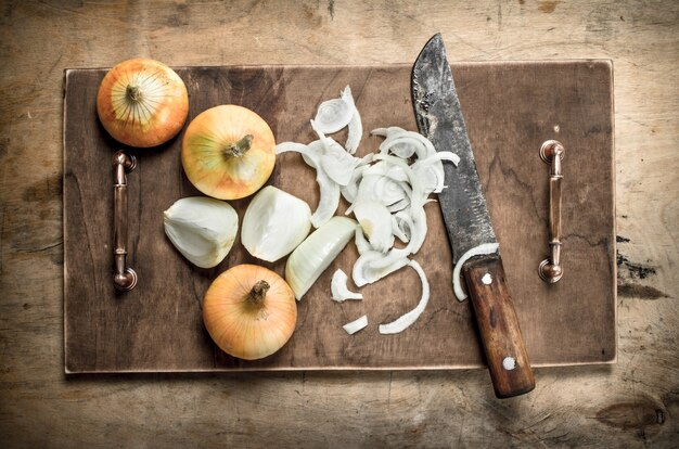 Cortando cebola fresca em uma tábua de cortar com uma faca velha em um fundo de madeira