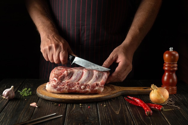 Cortando costelas cruas com açougueiro ou cozinheiro mãos na tábua de cozinha Churrasqueira Idéia para um menu de restaurante ou hotel em um fundo escuro