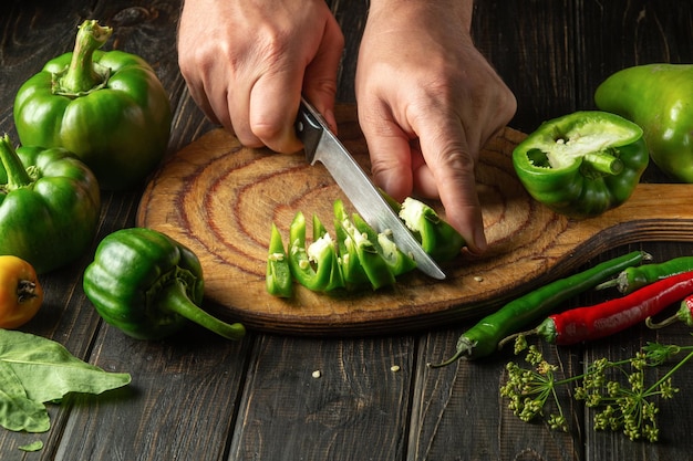 Cortando pimentões frescos verdes em uma tábua pelas mãos de um chef