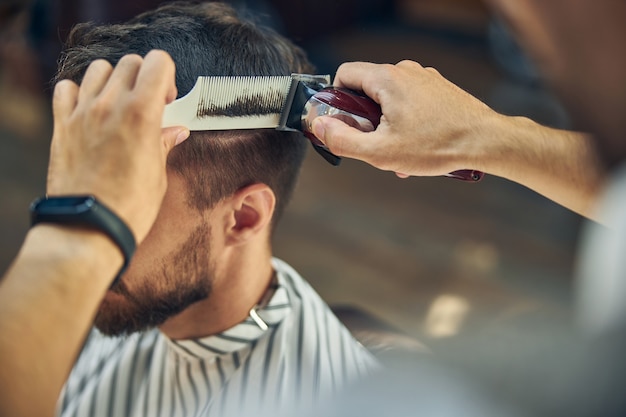 Foto cortapelos eléctrico y un peine en manos de un hábil peluquero