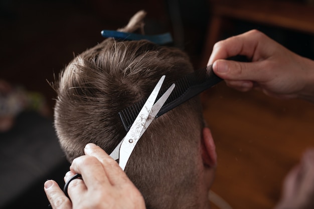 Cortar el cabello a mano con un peine y unas tijeras. El peluquero hace un peinado de moda para el cliente.