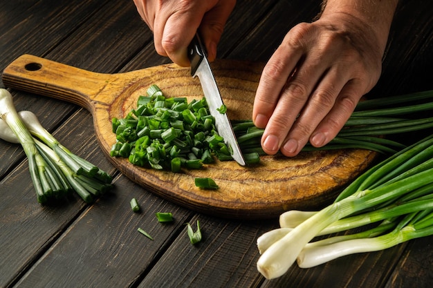 Cortar cebolas verdes em uma tábua de corte com uma faca para cozinhar comida vegetariana Prato camponês
