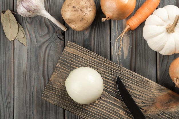 Cortar cebolla picante con un cuchillo en la tabla de madera de la cocina Cebolla blanca entera Vista plana Diseño de verduras en la mesa