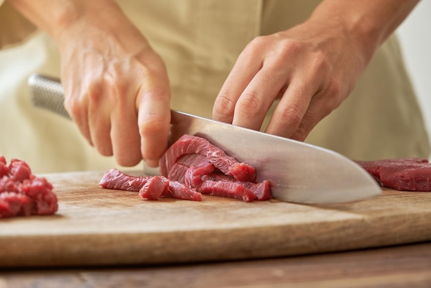 Cortar chef feminina profissional em processo de corte de carne em tábua de madeira com faca afiada enquanto cozinha