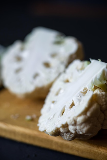 Cortar la coliflor por la mitad en una tabla de cortar Fondo oscuro Cocinar bistec de coliflor Concepto de dieta de comida vegetariana