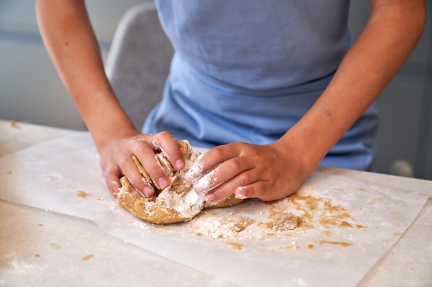 Cortar criança sem rosto amassando massa de biscoito crua com as mãos na mesa enquanto se prepara para assar na cozinha leve em casa