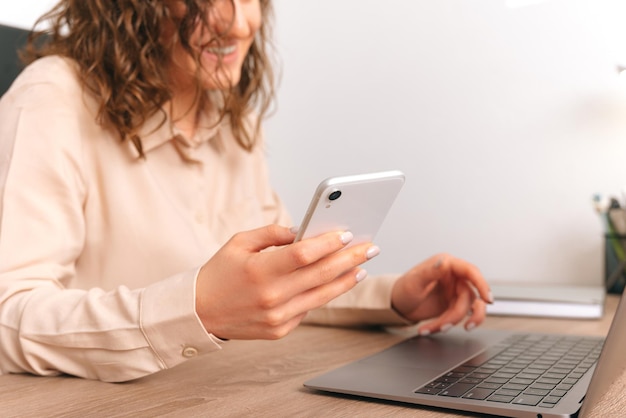 Cortar foto de uma jovem em êxtase usando telefone enquanto trabalhava no laptop no escritório