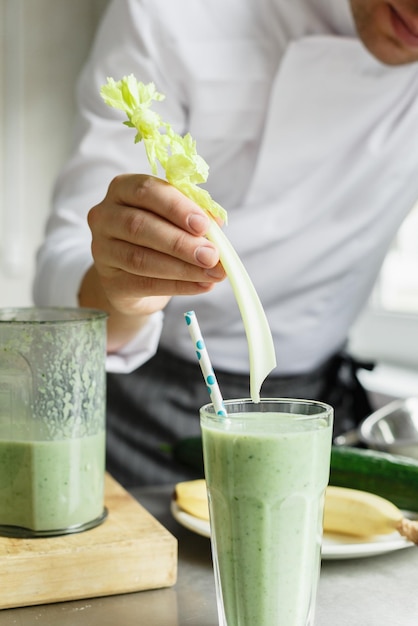 Cortar foto sem rosto do jovem chef masculino servindo copo de smoothie vegetal com aipo