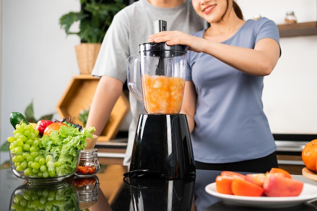 Cortar imagem de casal asiático feliz gosta de usar a máquina de liquidificador para fazer smoothie vegano saudável no balcão da cozinha Casal fazendo smoothie vegano juntos em casa para um estilo de vida saudável