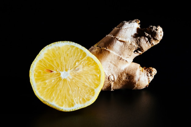 Cortar el limón y el jengibre aislado en una superficie negra, primer plano. Ingredientes útiles y vitaminas naturales.