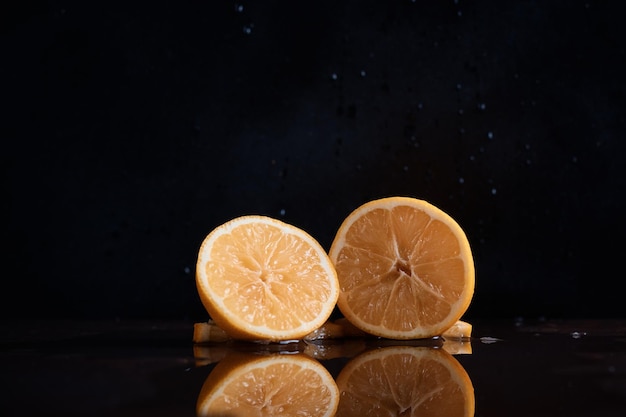 Cortar el limón en la mesa jugosas rodajas de cítricos frescos reflejados en el fondo oscuro del primer plano de vidrio