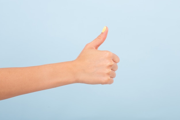 cortar mão feminina com manicure brilhante segurando o polegar para aprovar contra a luz natural