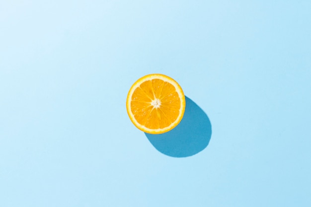 Cortar la mitad de naranja sobre una superficie azul. Minimalismo Concepto de trópicos, alimentación saludable, vitaminas. Vista plana, vista superior.