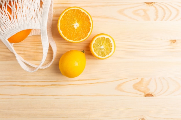 Cortar naranja y limón en algodón bolsa ecológica de compras sobre fondo de madera. Cosecha de cítricos, composición monocromática con copyspace