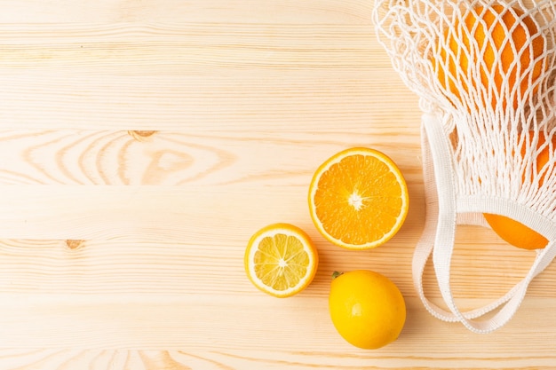 Cortar naranja y limón en algodón bolsa ecológica de compras sobre fondo de madera. Cosecha de cítricos, composición monocromática con copyspace