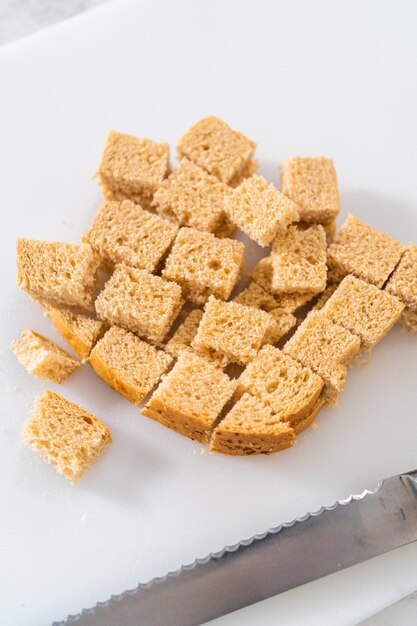 Cortar pão amanhecido com uma faca de pão em uma tábua branca para fazer croutons