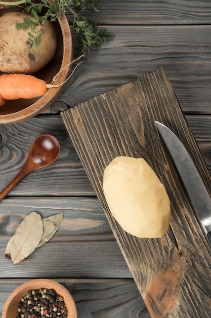 Cortar patatas crudas con un cuchillo en la tabla de madera de la cocina Patata fresca entera pelada cocina tradicional Vista plana