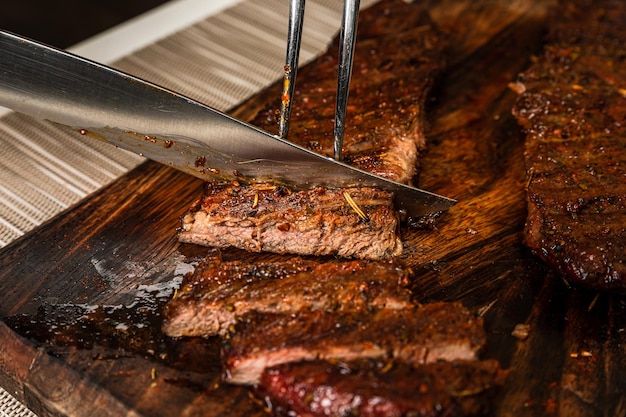 Cortar pedaço grelhado cozido de carne de bife de denver na tábua de madeira com uma faca closeup