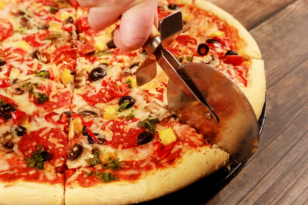 Cortar pizza assada com azeitona, cogumelos, calabresa e queijo.