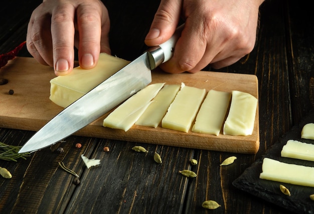 Cortar queijo mozzarella em uma tábua de cozinha faca na mão do cozinheiro