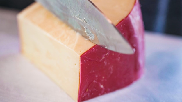 Cortar queso gouda en cubos pequeños sobre una tabla de cortar blanca.