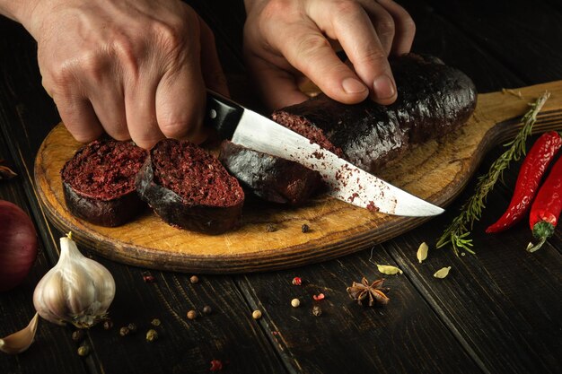 Cortar salchichas de sangre con las manos de un chef en una tabla de cortar Cocinar un plato nacional en la mesa de la cocina