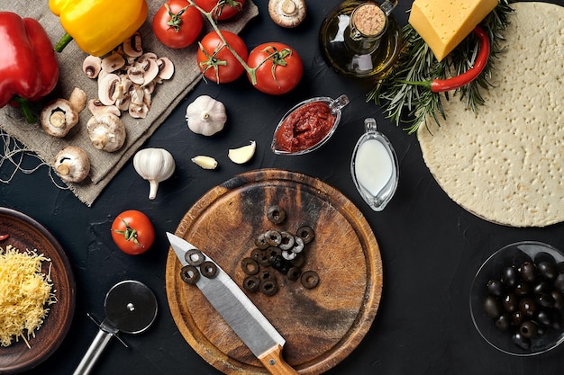 Foto cortar tablero de madera con ingredientes tradicionales de preparación de pizza queso salsa de tomate aceitunas aceite de oliva pimienta especias fondo de mesa de textura negra