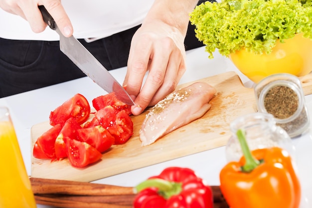 Cortar tomate y pechuga de pollo en la tabla de cortar.