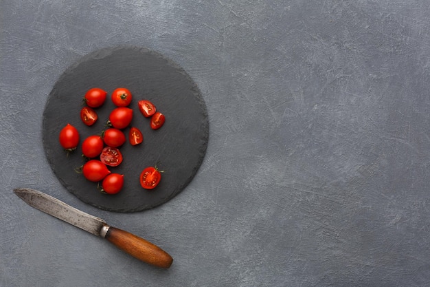 Cortar los tomates en una placa rústica de piedra pizarra. Cocinar alimentos saludables sobre fondo gris, espacio de copia, vista superior.