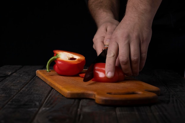 Cortar verduras Manos masculinas cortando pimienta roja dulce en la tabla de cortar