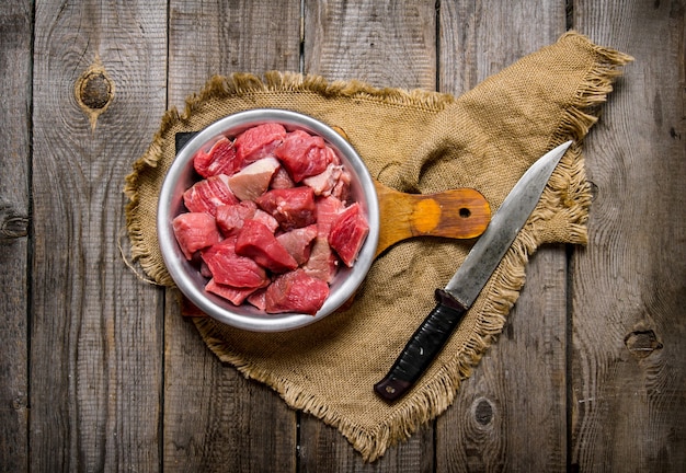 Corte a carne crua com uma faca grande. Na mesa de madeira.