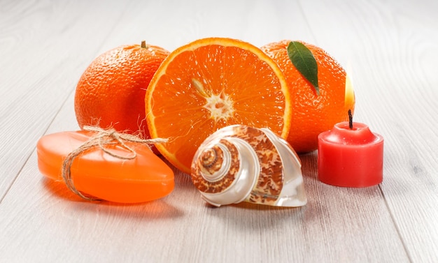 Corte a laranja com duas laranjas inteiras, sabão, concha do mar e vela vermelha acesa na mesa de madeira. Produtos e acessórios de spa.