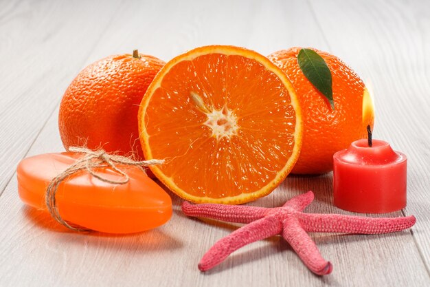 Corte a laranja com duas laranjas inteiras, sabão, estrela do mar e uma vela acesa na mesa de madeira. Produtos e acessórios de spa