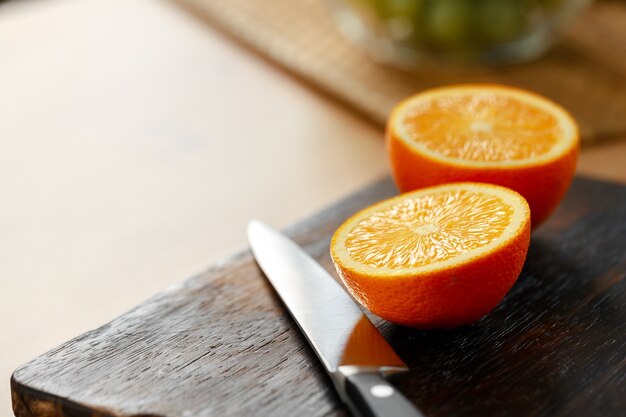 Corte a laranja e a faca na tábua de madeira na mesa