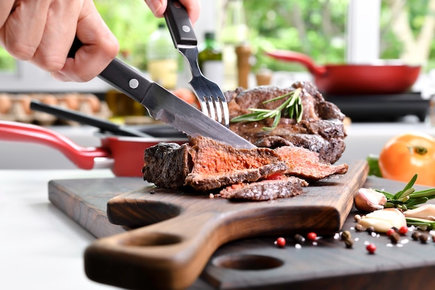 Corte à mão bifes grelhados com especiarias numa tábua de madeira na cozinha