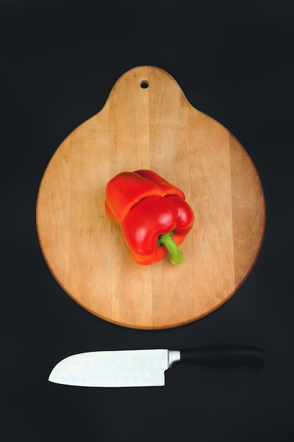 Corte a pimenta vermelha na placa de madeira e fundo preto