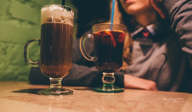 Corte a visão da mulher sentar na mesa. café com leite com chantilly e vinho quente em taças.