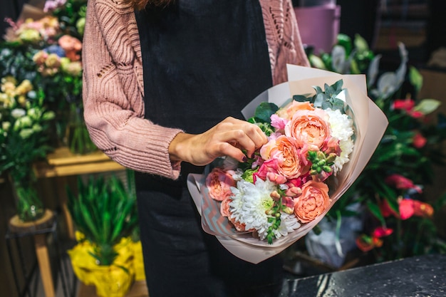 Corte a vista da florista feminina segurando lindo buquê nas mãos. Ela toca uma flor. Outros buquês estão atrás dela.