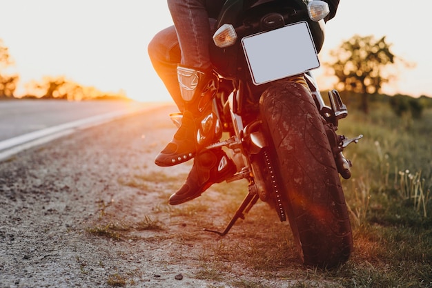 Foto corte a vista das pernas do motociclista sentado na bicicleta enquanto viaja ao redor do mundo contra o pôr do sol.