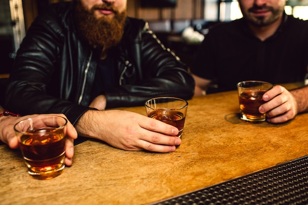 Corte a vista de três homens sentados no balcão de bar. Eles seguram copos com rum. Caras são sérios.