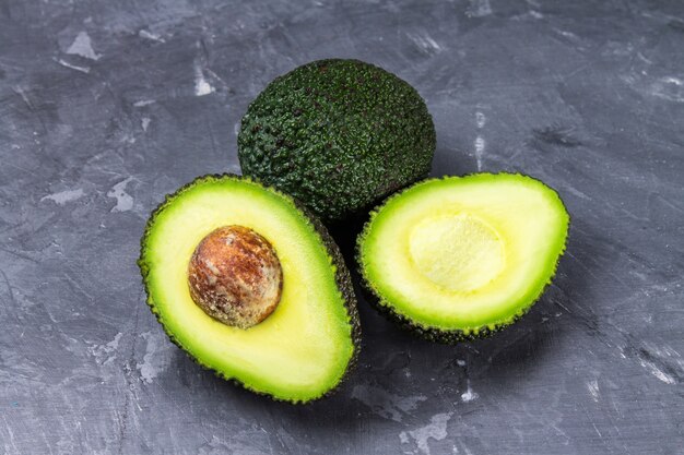 Corte y aguacate entero en un tablero de madera en un fondo gris.