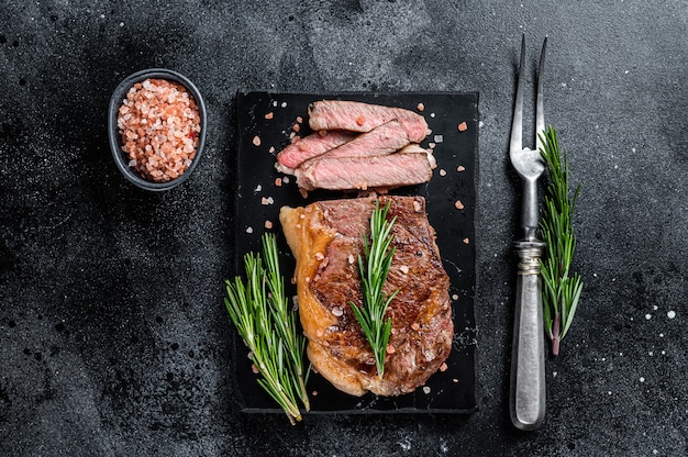 Corte el bistec o el lomo de carne de vacuno asado en tiras de New York en una tabla de mármol