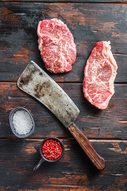 Corte de carne orgánica de hoja superior, filete de ternera cruda marmolada, con cuchillo de carnicero y condimentos en la mesa rústica de madera oscura.