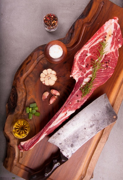 Corte de costilla corta de carne cruda marmolada con grasa y hueso en piedra con especias y cuchilla en el retrato de la vista superior de la tabla de madera