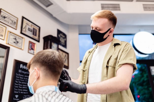 Corte de cabelo de homem em uma barbearia. Cliente e barbeiro com máscaras antivírus. Corte de cabelo em quarentena.