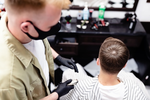 Corte de cabelo de homem em uma barbearia. cuidado capilar. barbeiro e cliente em máscara contra vírus. corte de cabelo em