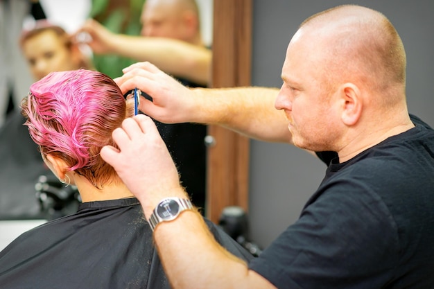 Corte de cabelo tingido de cabelo molhado rosa curto de jovem caucasiana por um cabeleireiro masculino em uma barbearia