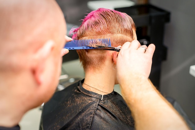 Corte de cabelo tingido de cabelo molhado rosa curto de jovem caucasiana por um cabeleireiro masculino em uma barbearia