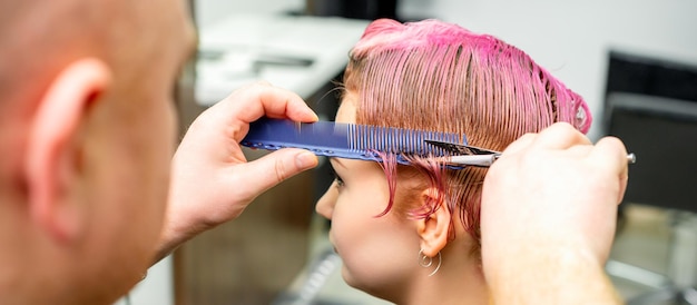 Corte de cabelo tingido de cabelo molhado rosa curto de jovem caucasiana por um cabeleireiro masculino em uma barbearia