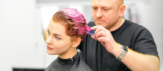 Corte de cabelo tingido de cabelo molhado rosa curto de jovem caucasiana por um cabeleireiro masculino em uma barbearia